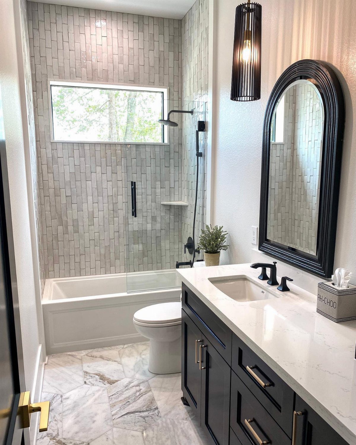White bathtub with black rainfall showerhead and grey vertical wall tiles in bathroom.