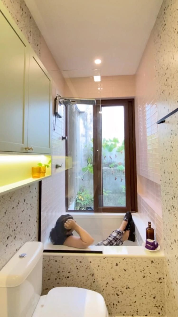 Small bathroom with a white bathtub, terrazzo walls, and a window to outdoors.