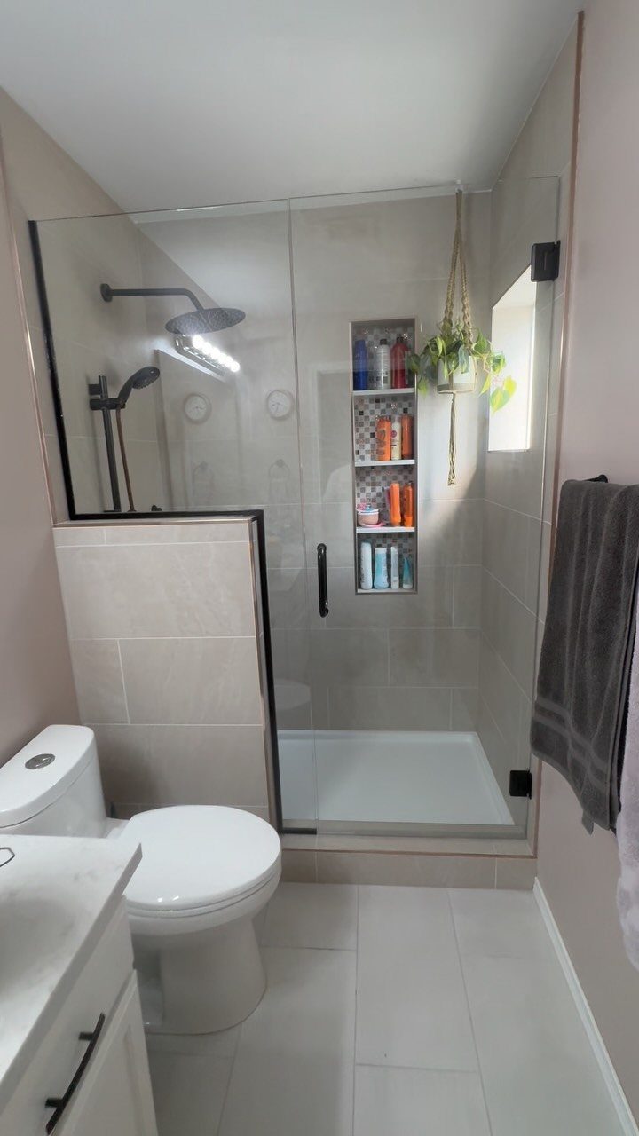 Glass-enclosed alcove shower with recessed storage niche in a small white bathroom.