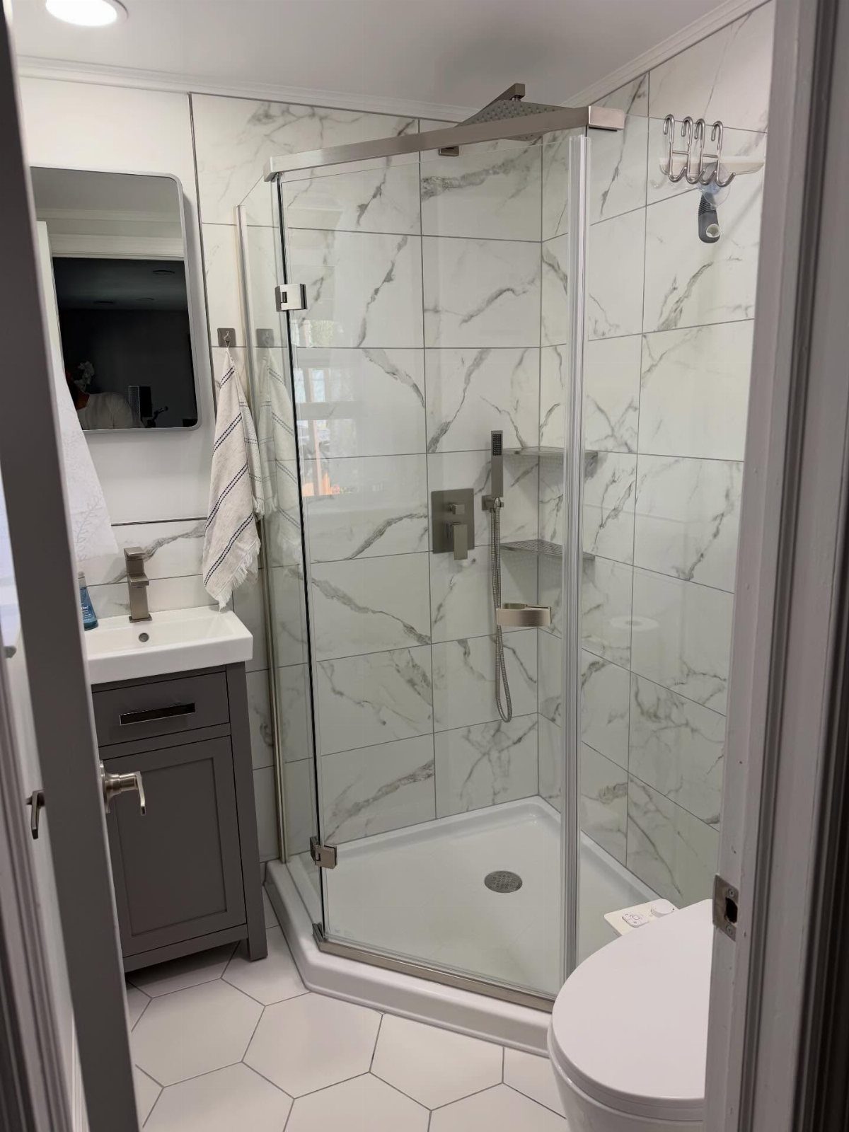 Corner shower with glass enclosure and marble tiles in a small white bathroom.