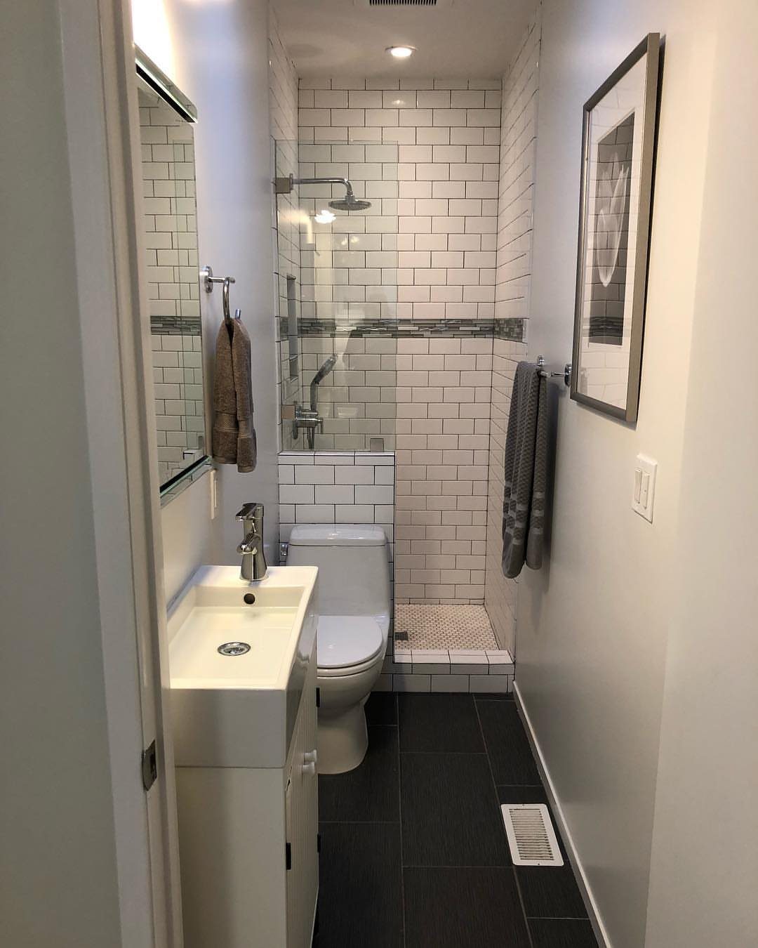 Narrow bathroom with white subway tiles, white fixtures, and dark floor tiles.