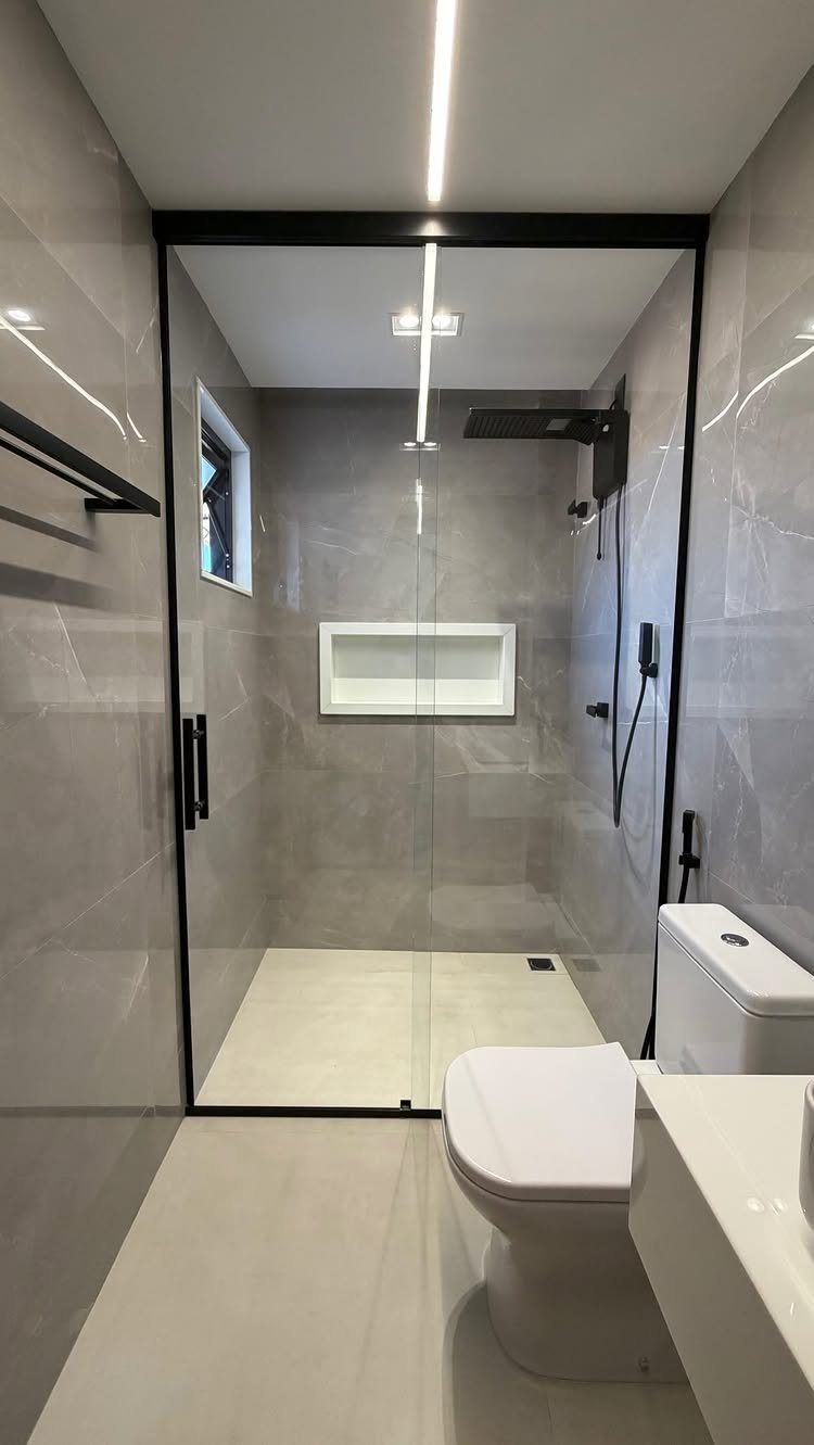 Modern small bathroom with light grey tiles, black shower frame, and black fixtures.