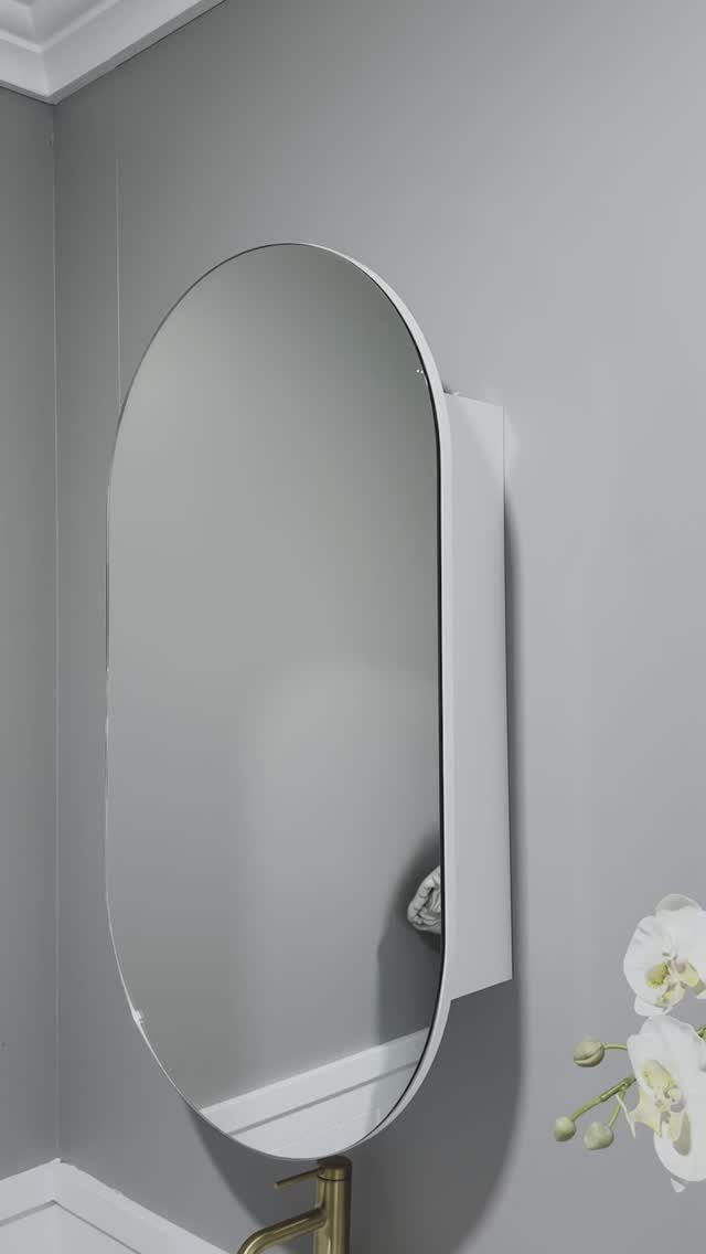 Oval mirrored cabinet mounted on a grey bathroom wall with gold faucet below.