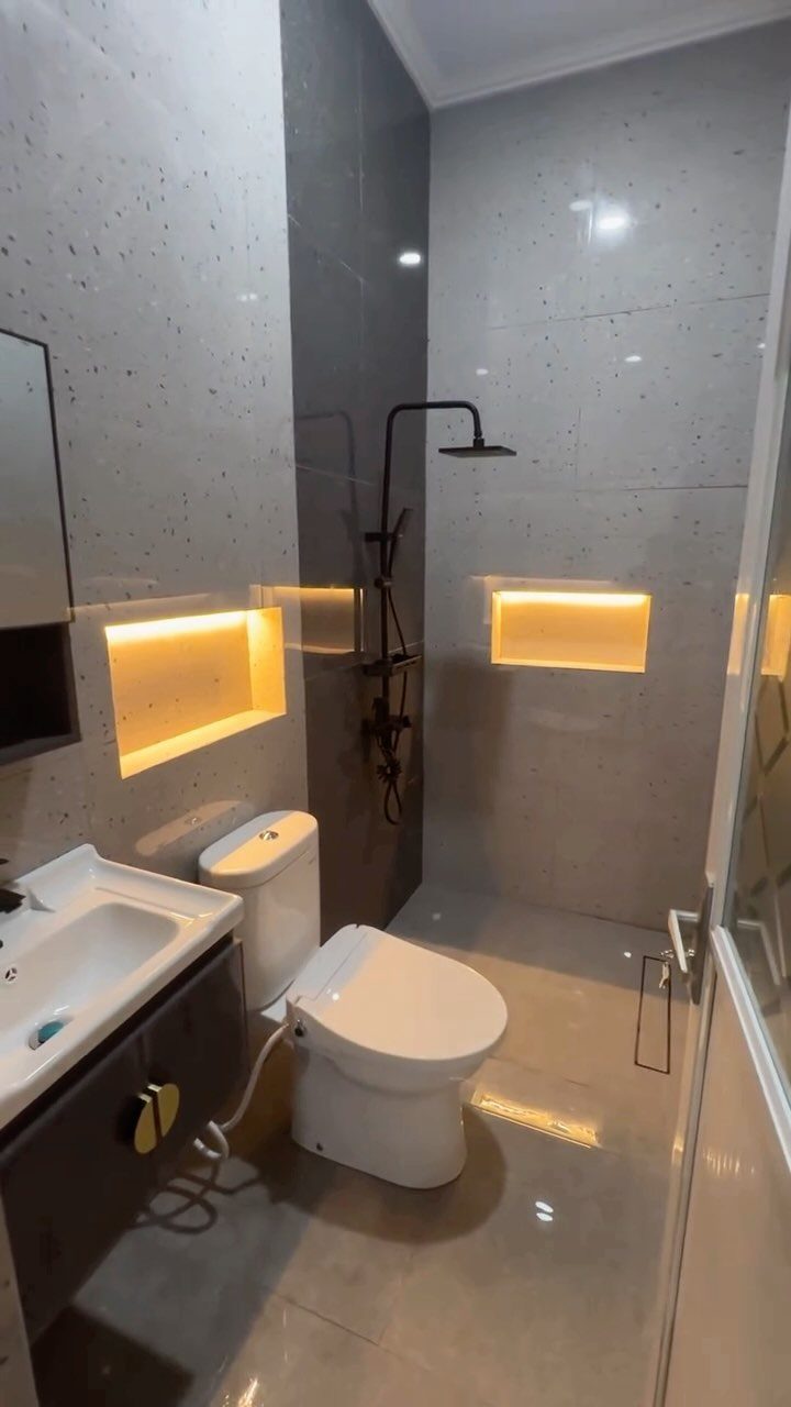 Modern small bathroom with grey tiles, black shower fixtures, and illuminated wall niches.