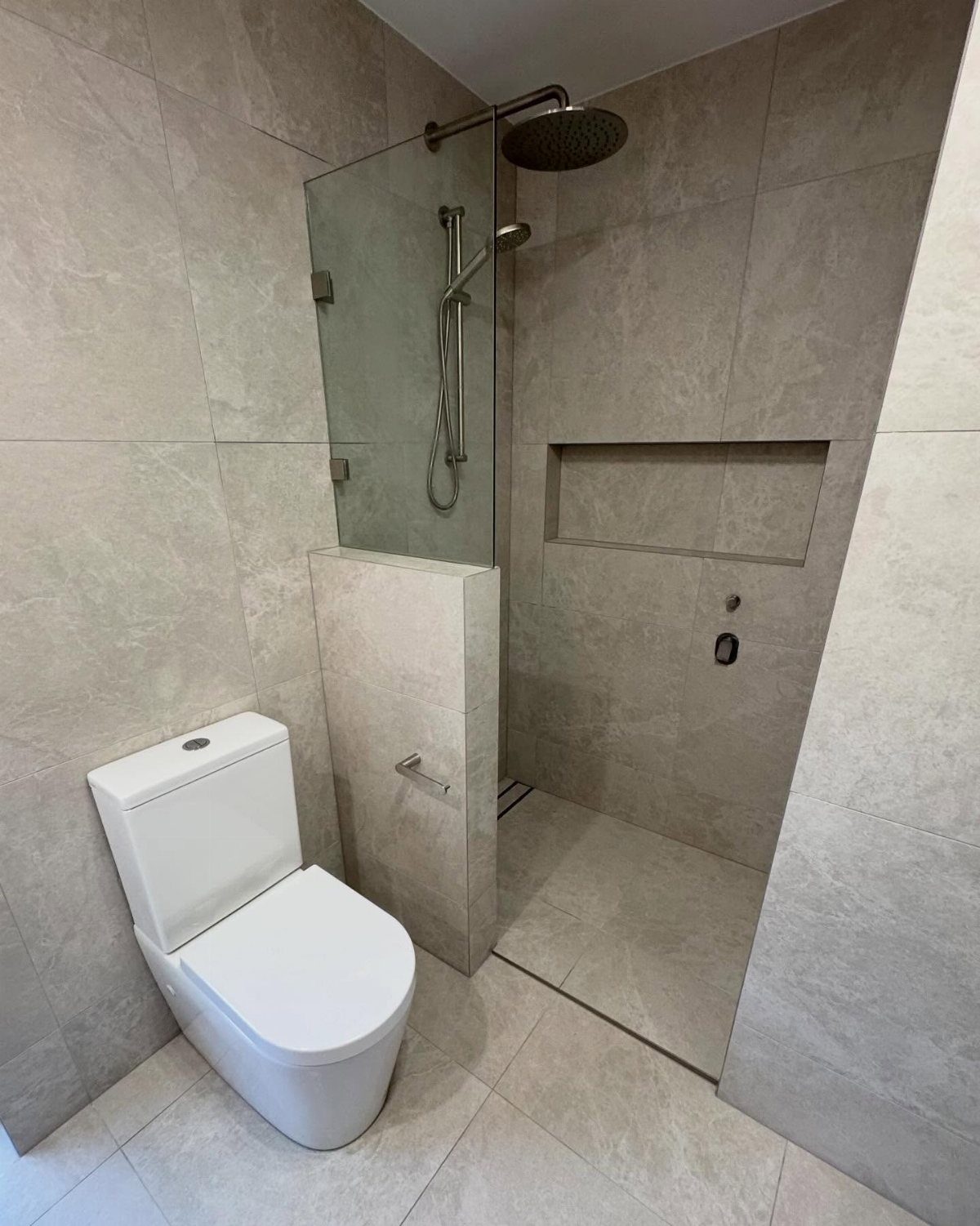 Small bathroom with beige tiles, white toilet, and a low shower partition wall.