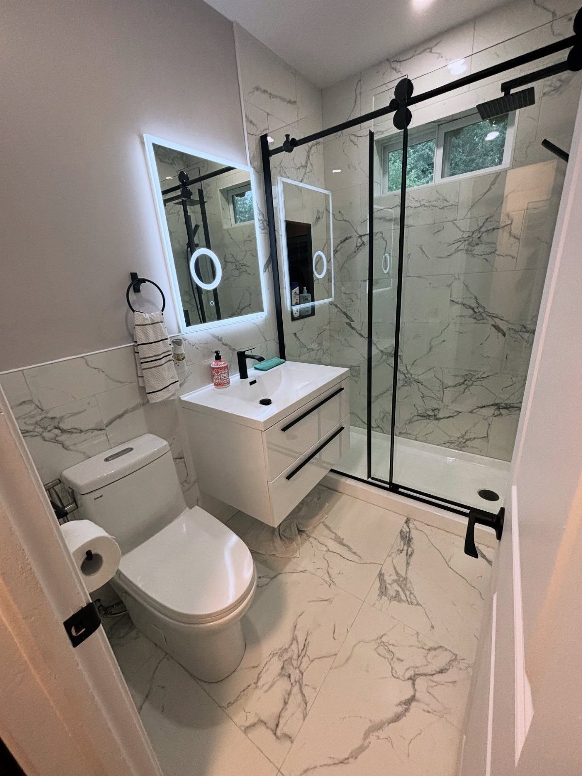 Small bathroom with white marble tiles, black fixtures, and sliding glass shower doors.