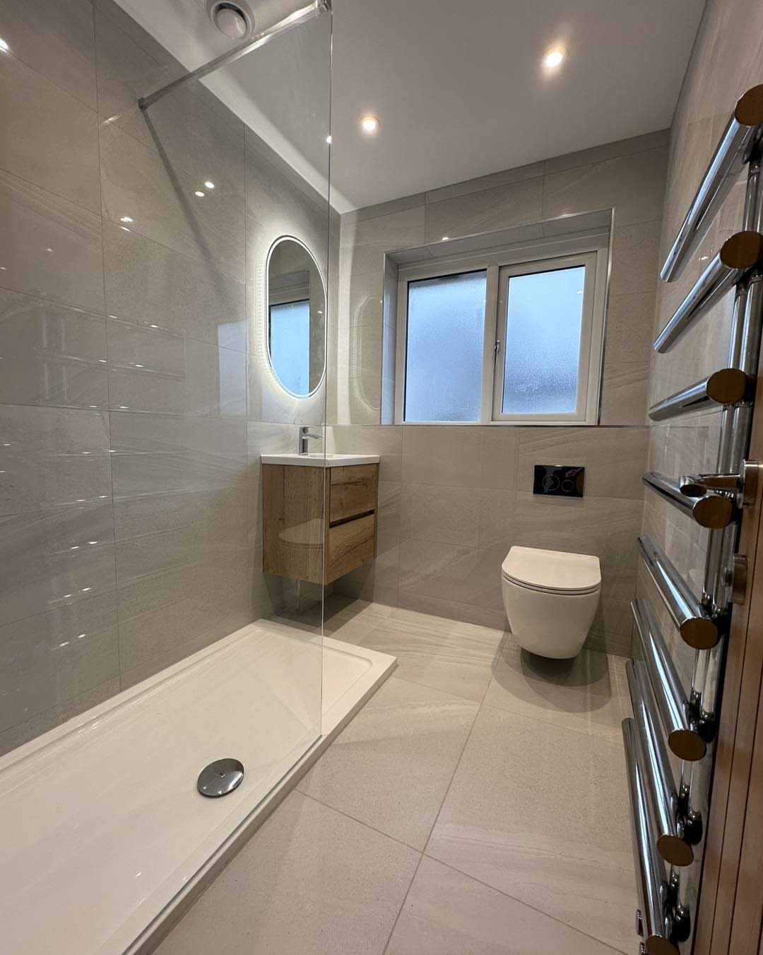 Modern small bathroom featuring recessed ceiling spotlights, light grey tiles, and walk-in shower.
