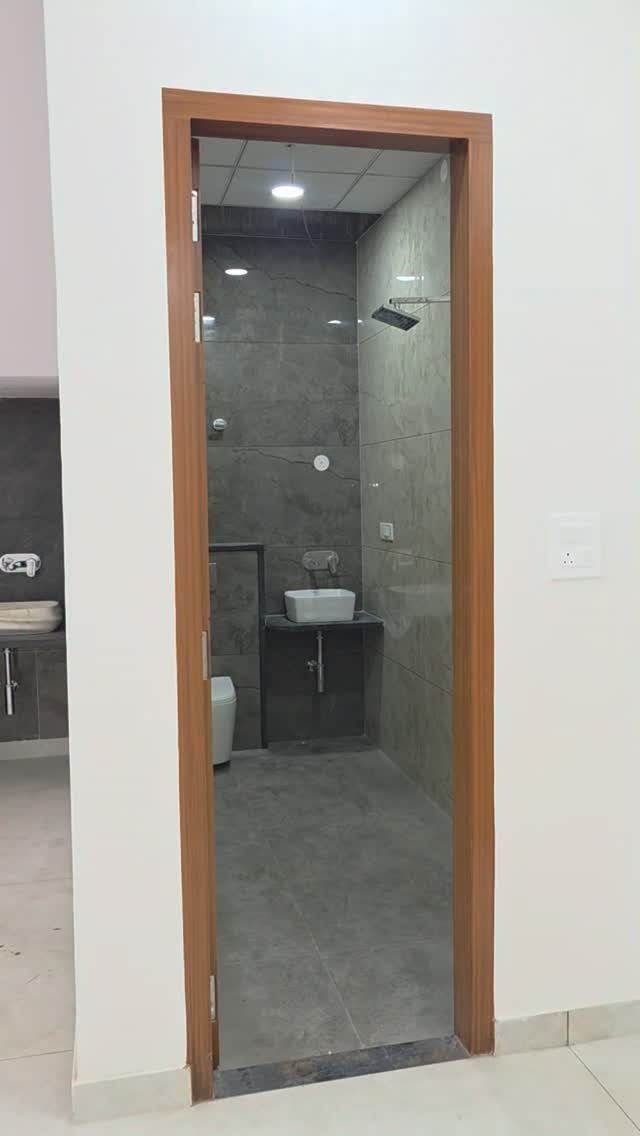 Small bathroom with grey stone tiles, wall-mounted sink, and open shower area.