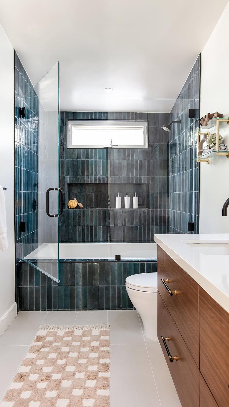 White alcove bathtub with dark blue vertical tiles and a frameless glass panel.