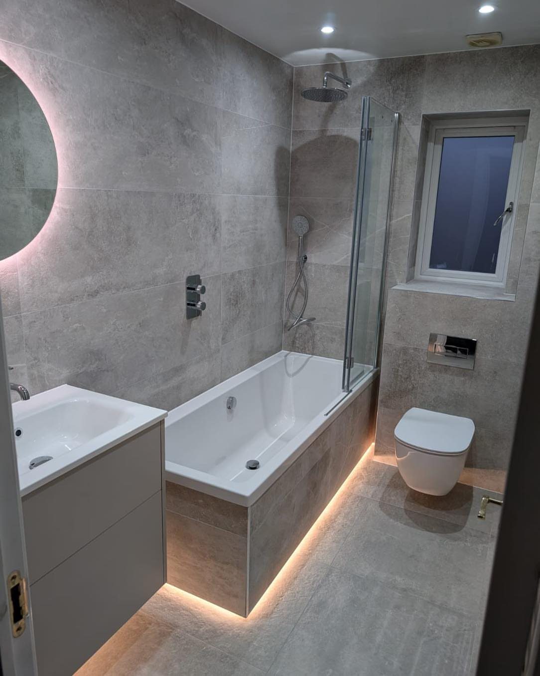 Modern small bathroom with light grey tiles, white bathtub, and floating vanity.