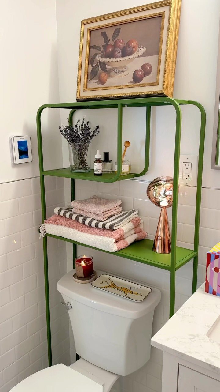 Green metal over-the-toilet storage shelves holding towels and toiletries in a white bathroom.