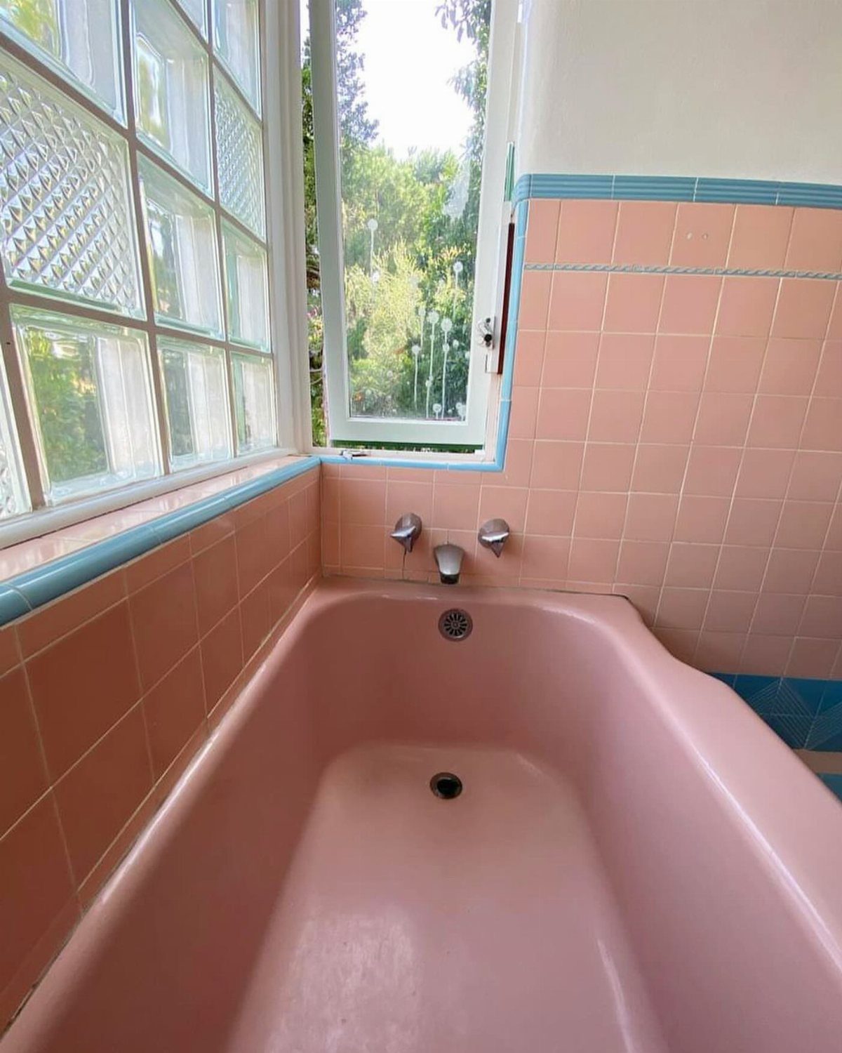 Pink bathtub and tiled walls next to glass block and clear windows.