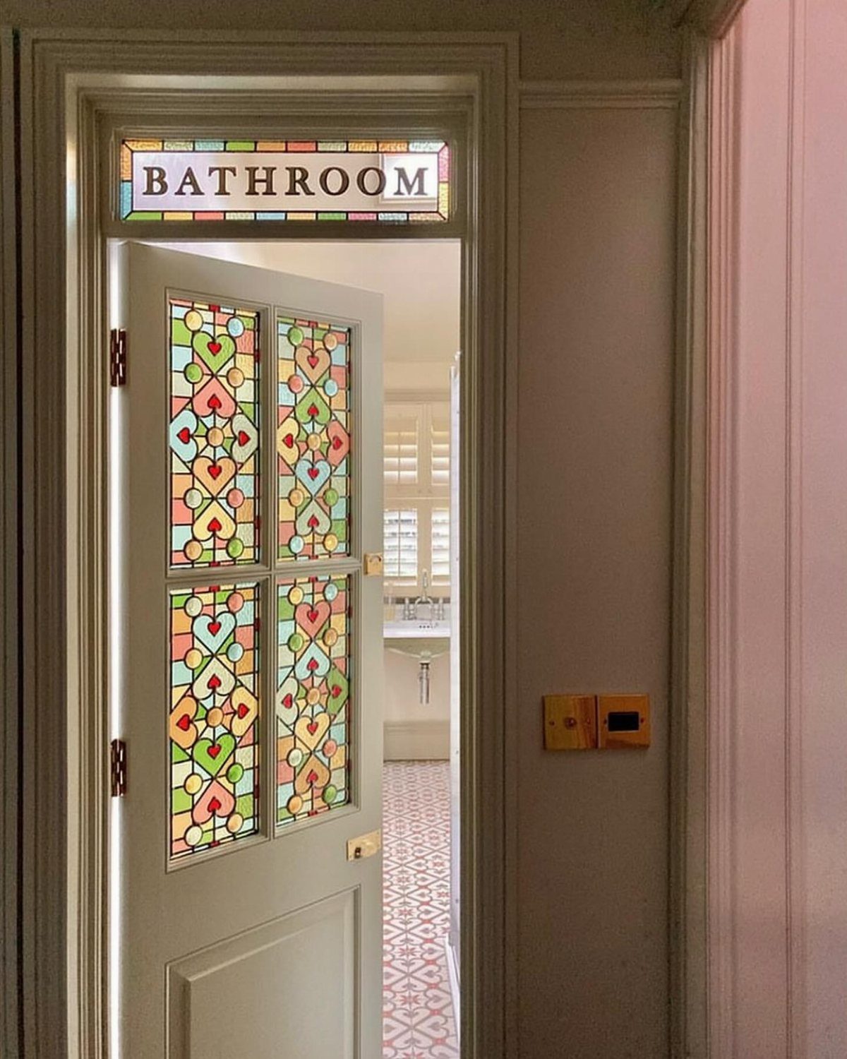 White bathroom door with colorful stained glass panels and a bathroom sign above.