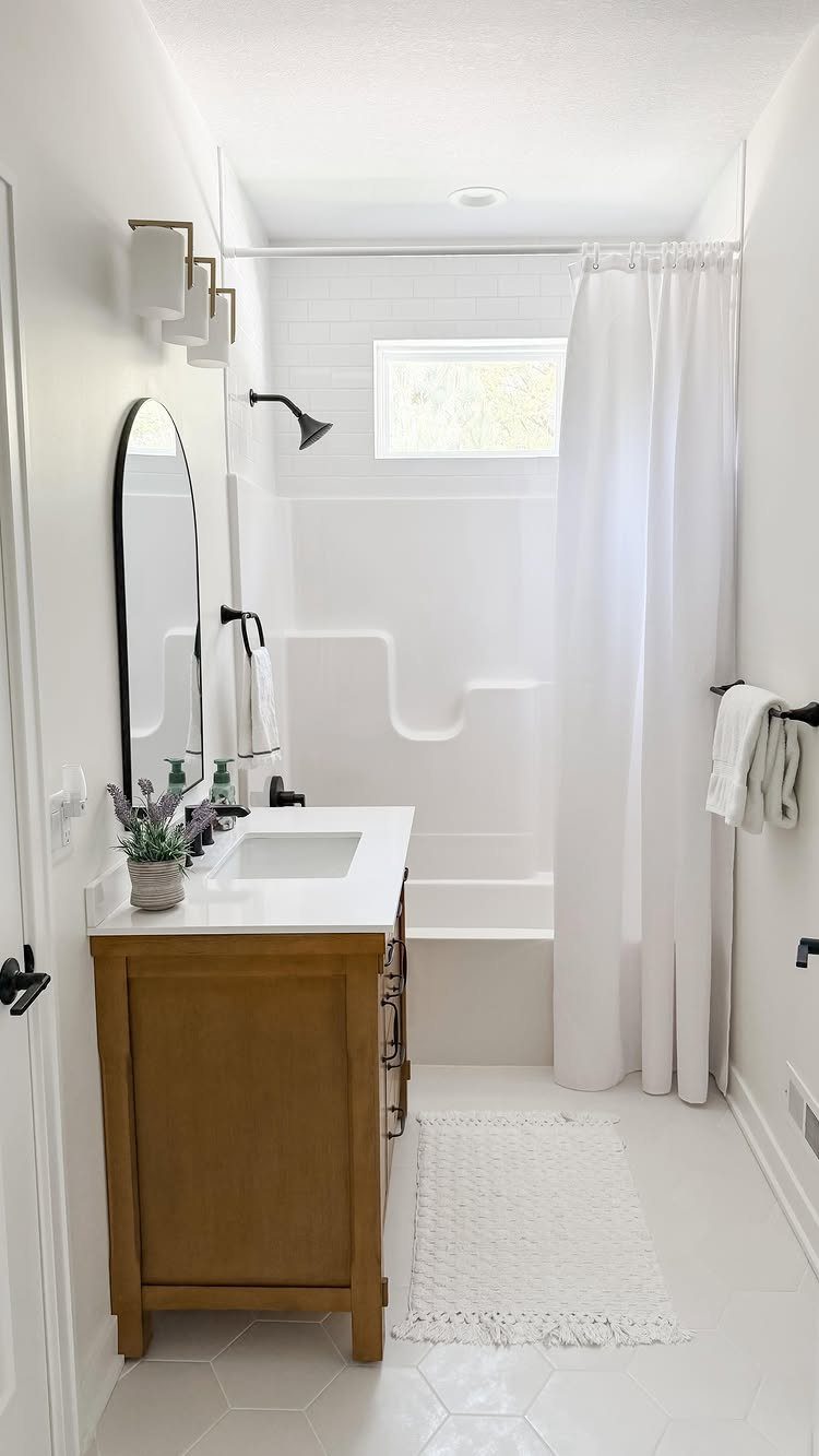 Small white bathroom with a wooden vanity and a high transom window.