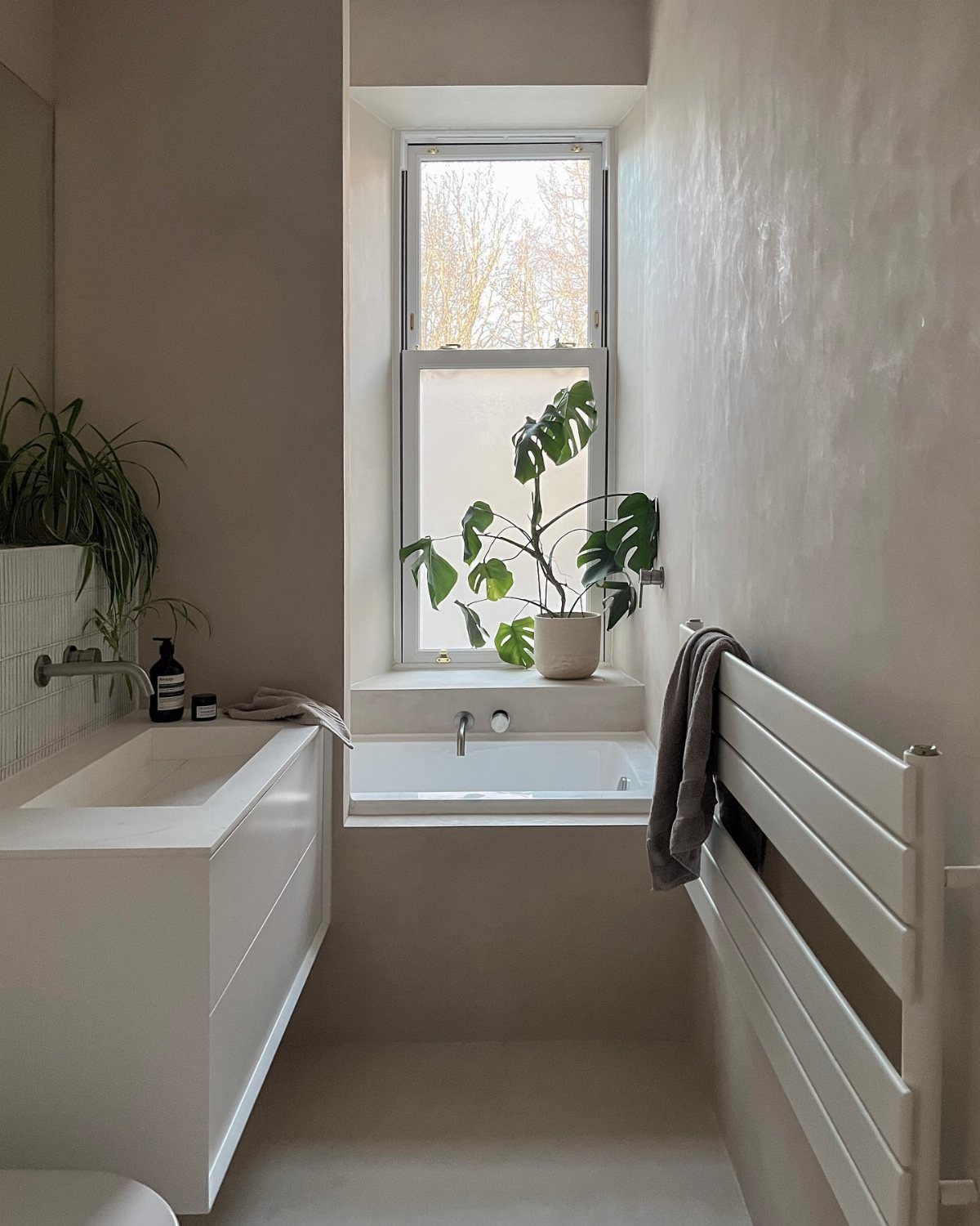 Small minimalist bathroom featuring a white bathtub under a window with a potted plant.