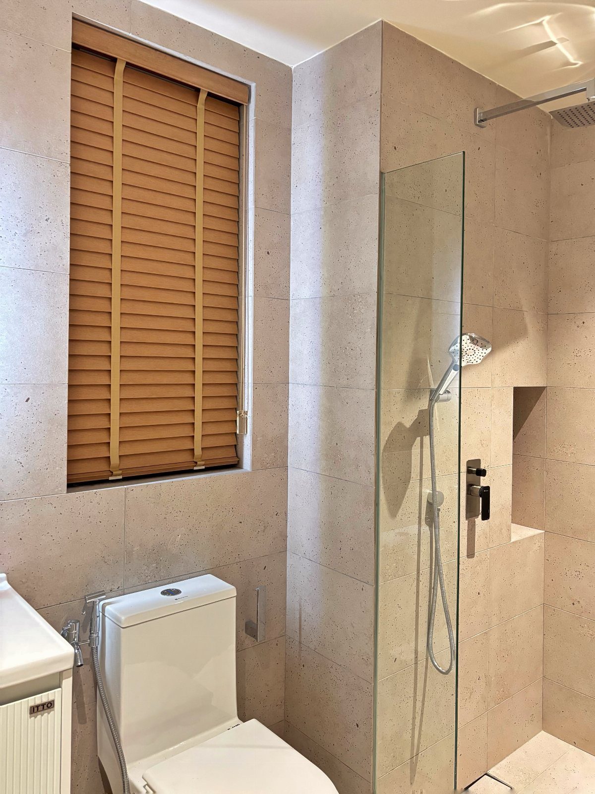 Small bathroom with beige tiles, white toilet, and window with brown wooden blinds.
