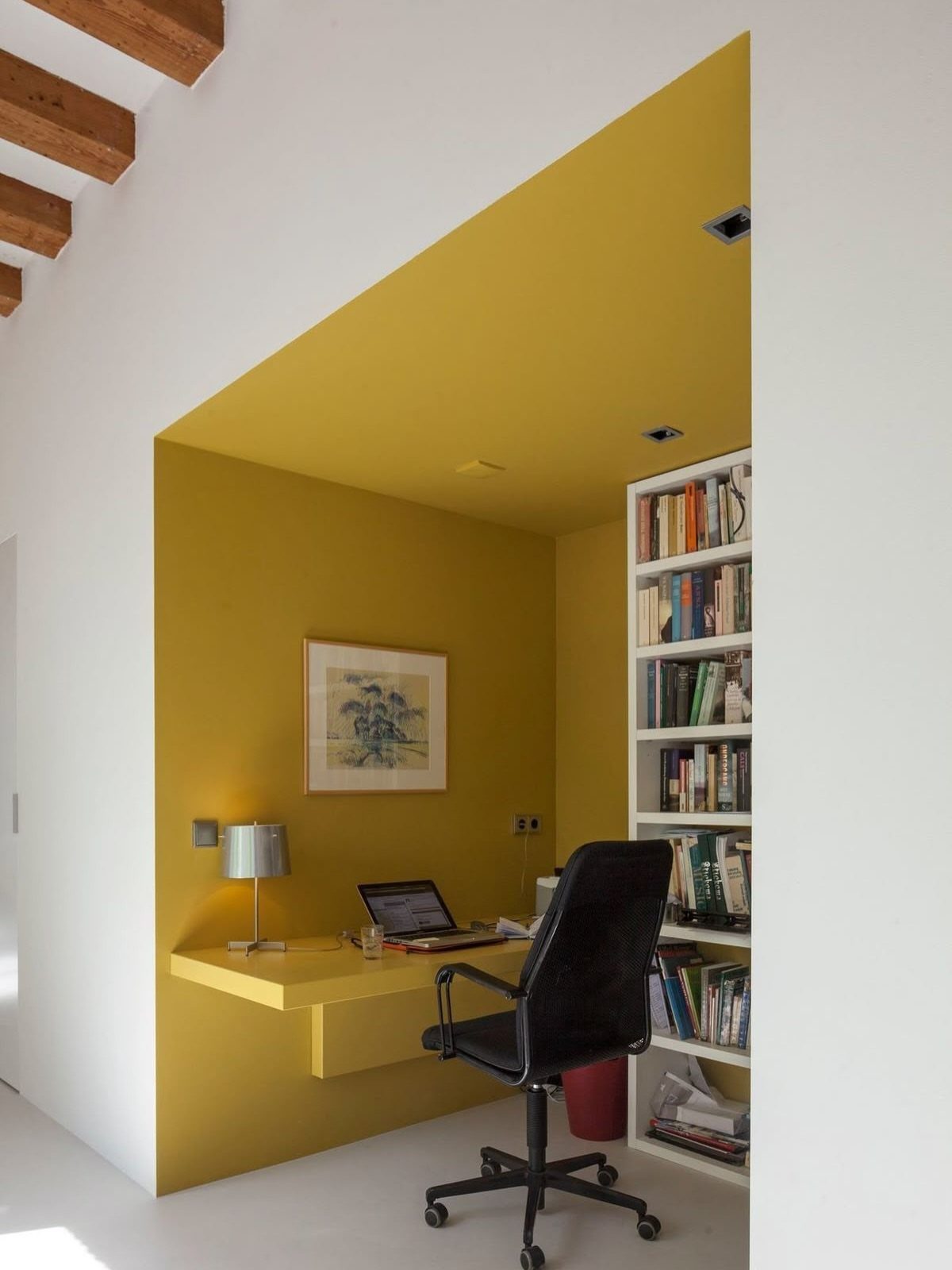 Yellow home office nook with built-in desk and bookshelf inside a white room.