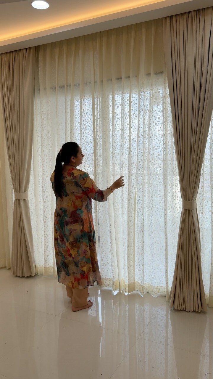 Woman standing by high beige curtains and sheer white drapes in a bright room