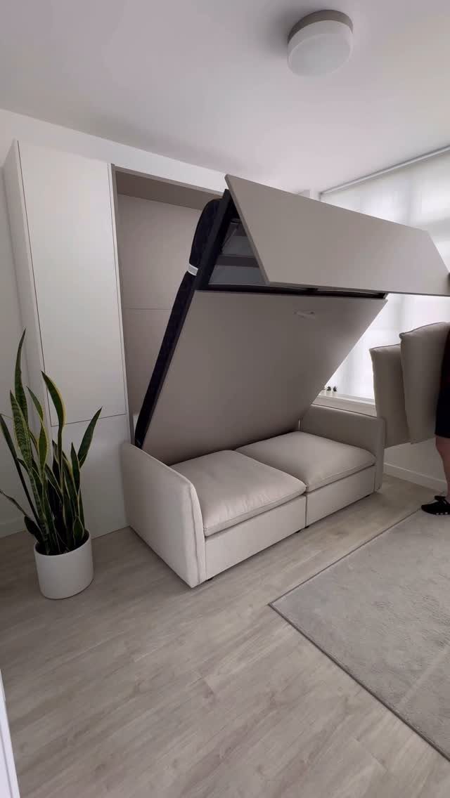 Beige Murphy bed partially folded into a white wall unit with integrated sofa.