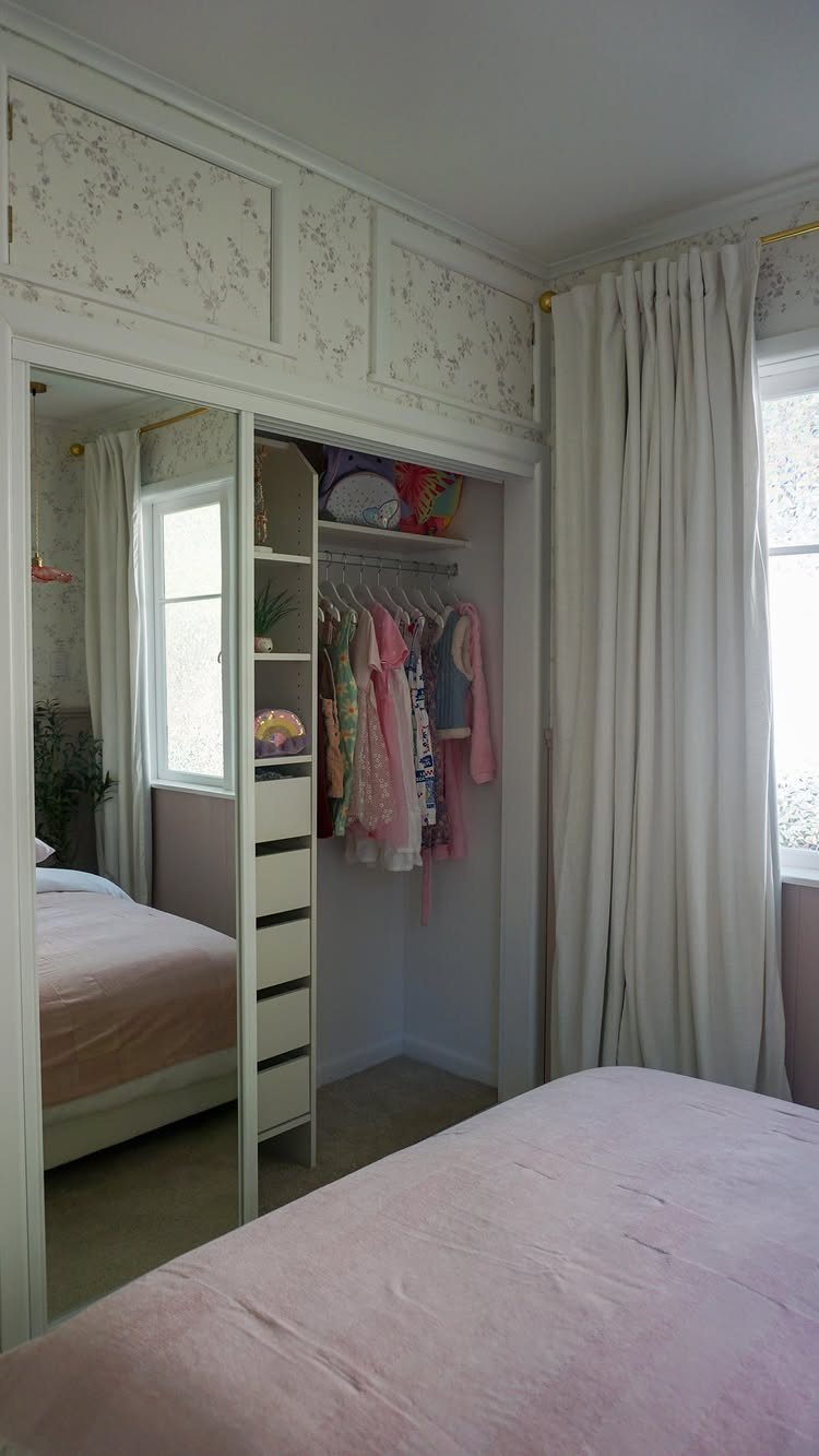 White built-in wardrobe with mirrored door and hanging clothes in a small bedroom