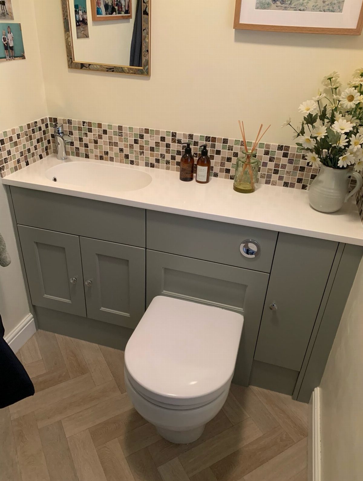 Grey bathroom vanity with white countertop, mosaic tiles, and floral arrangement.
