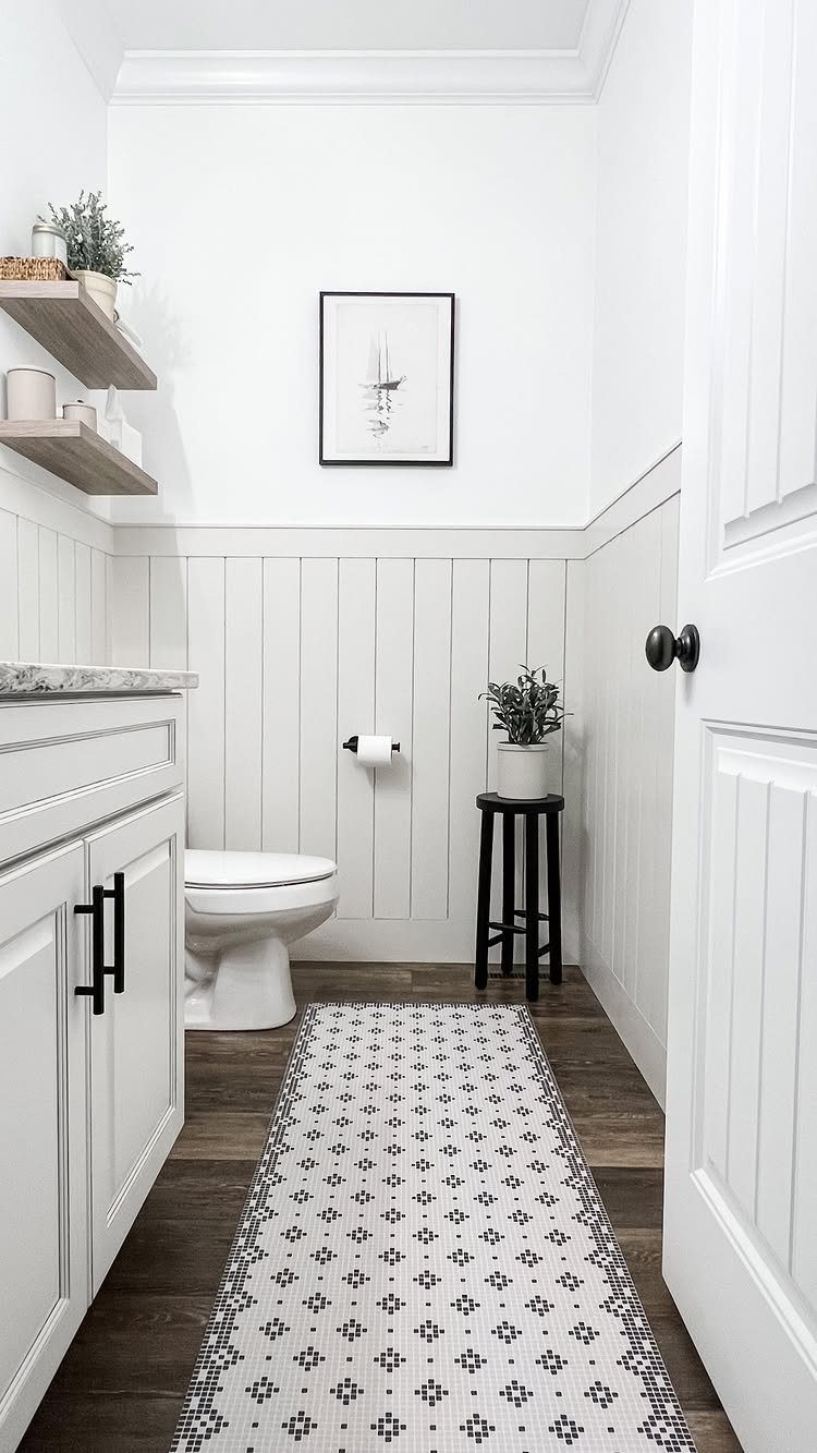 Small white bathroom with neutral tones, white wainscoting, and a patterned runner rug.