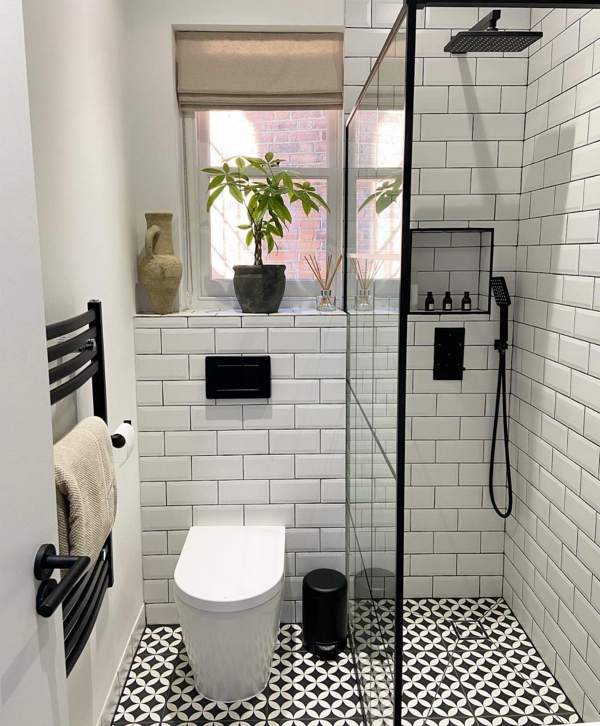 Small bathroom with white subway tiles, patterned flooring, and a black shower frame.