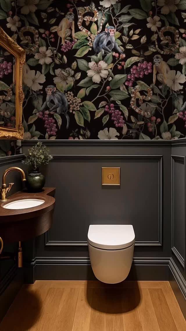 Dark floral wallpaper with monkeys above a grey wainscoted wall in a bathroom.
