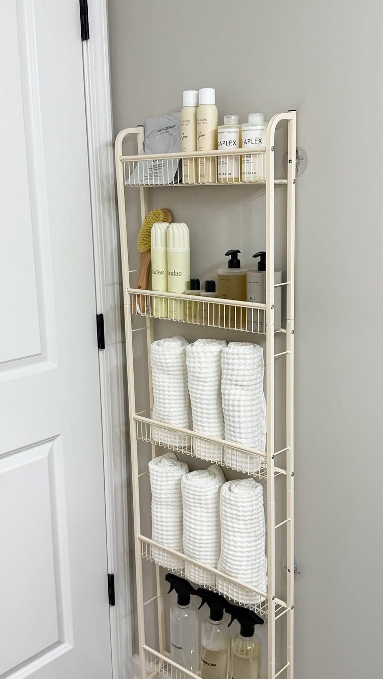 Cream metal wall-mounted shelves holding white towels and toiletries in a neutral bathroom.