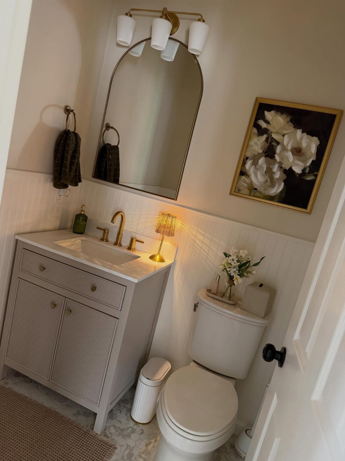 Gold wall sconces with white shades above an arched mirror in a bathroom