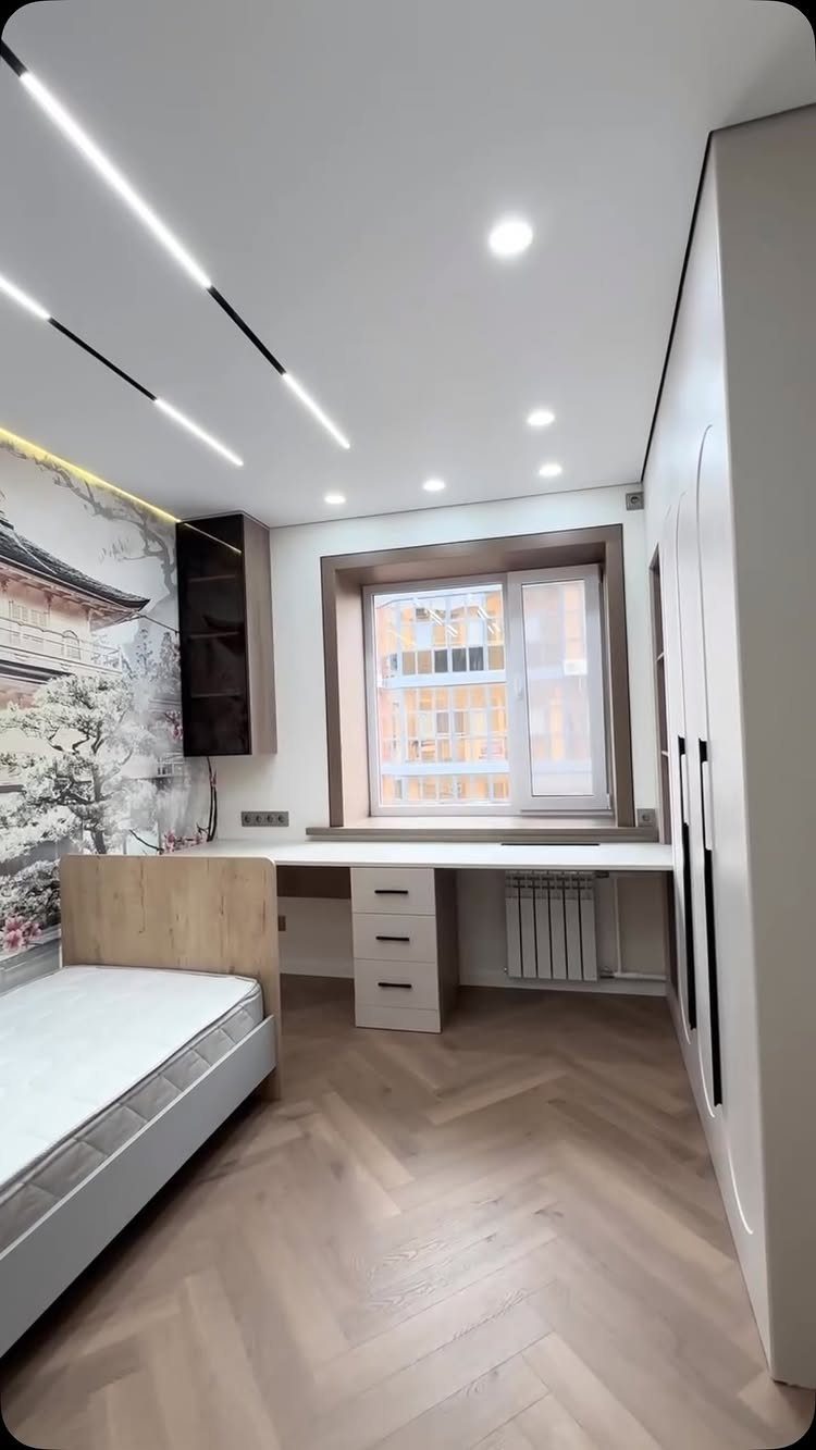 Small bedroom featuring a built-in desk under a window and a tall wardrobe.