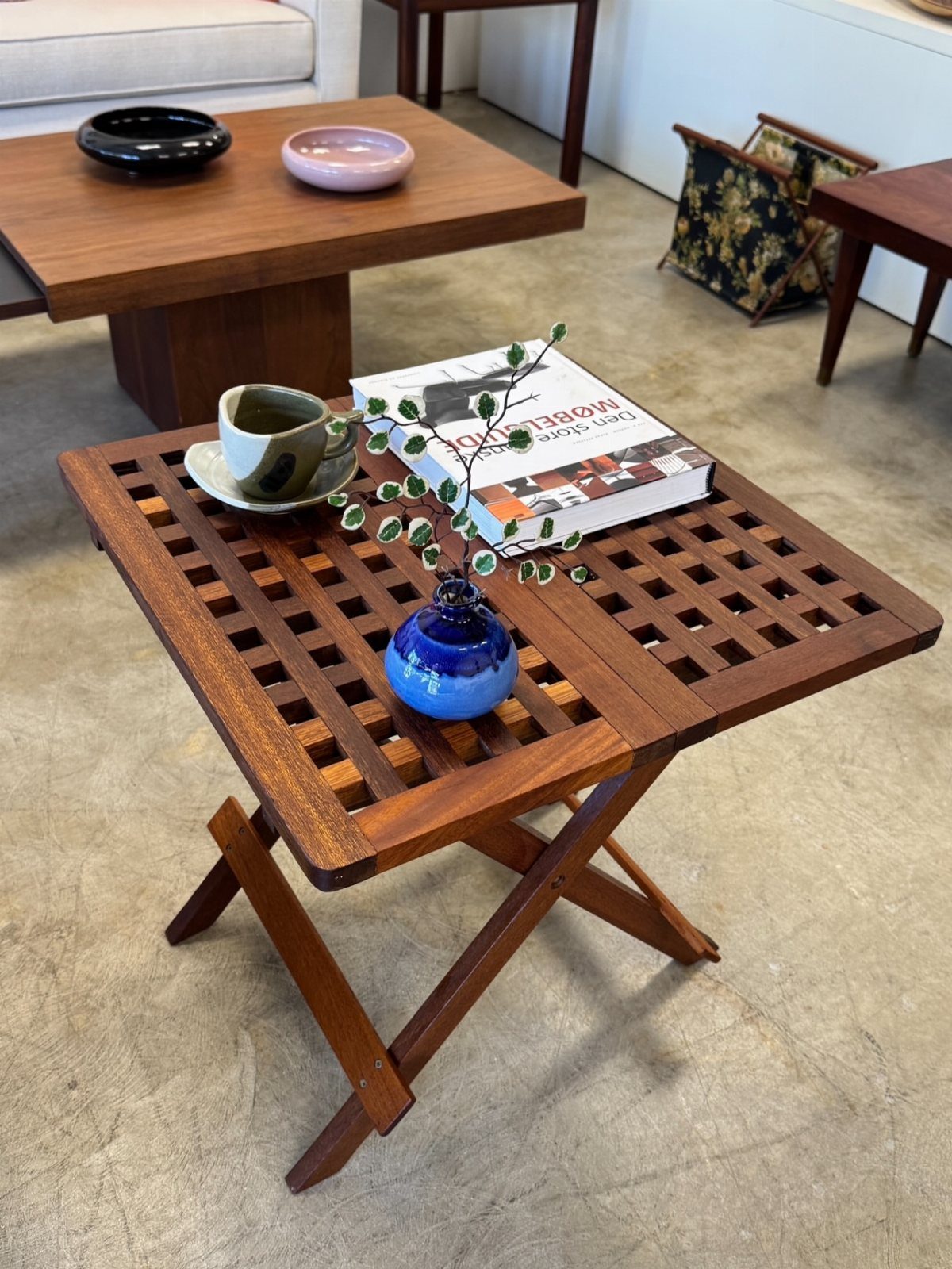Wooden slatted coffee table with a book, blue vase, and coffee cup.