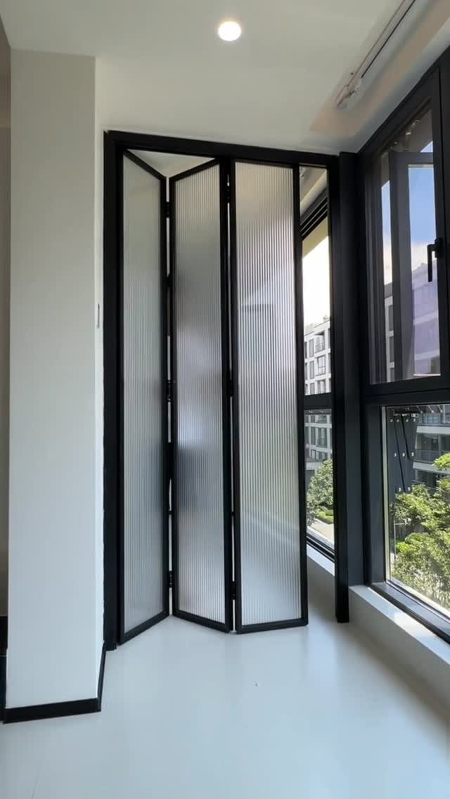 Black-framed folding frosted glass door in a modern white room with large windows.