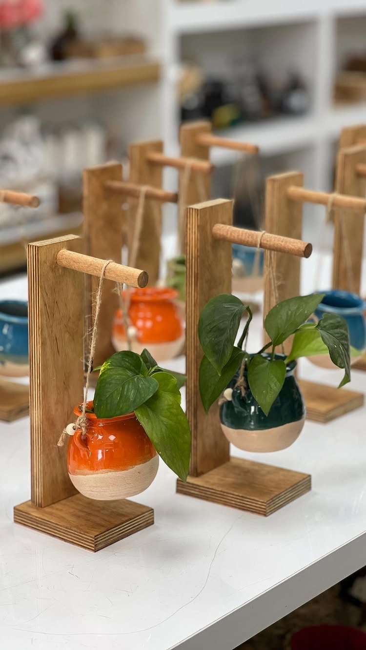 Wooden plant stands holding suspended orange and green ceramic pots with leafy plants.