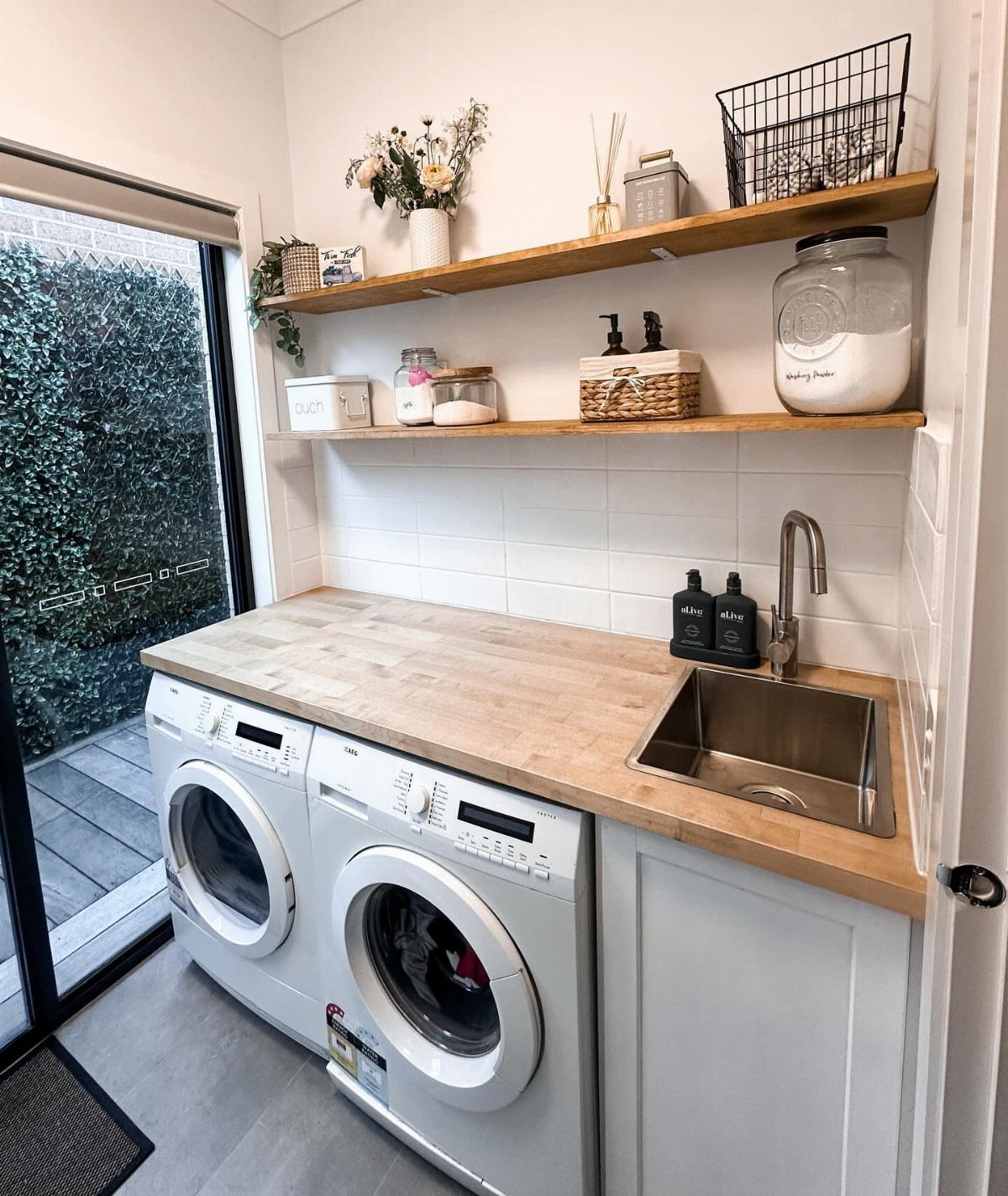 Laundry room with white washing machines, wood countertop, and wooden open wall shelves.