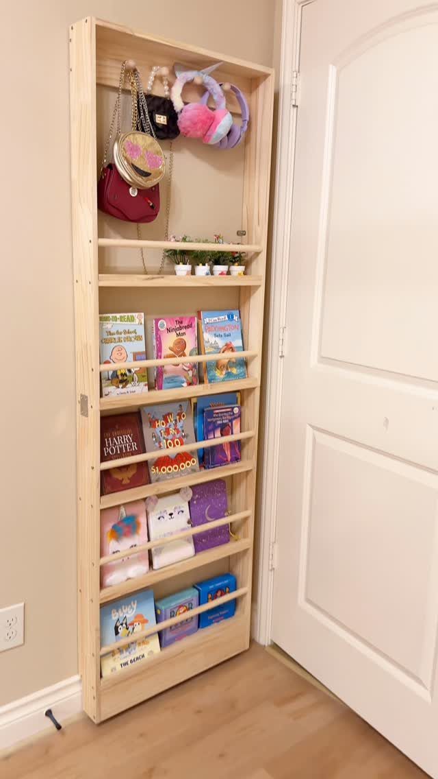 Tall narrow wooden shelving unit holding books and accessories against a white wall.
