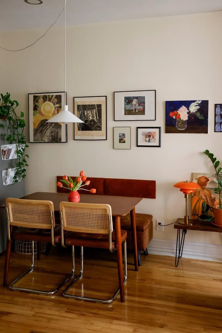 Small dining area with wooden table, cane chairs, and art on white walls.