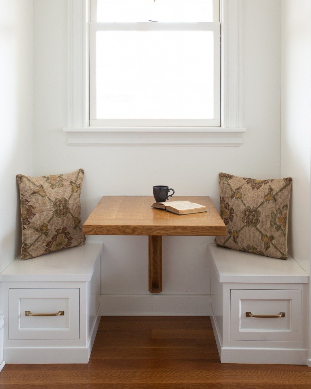 Built-in white storage benches and a wooden table in a bright window nook.