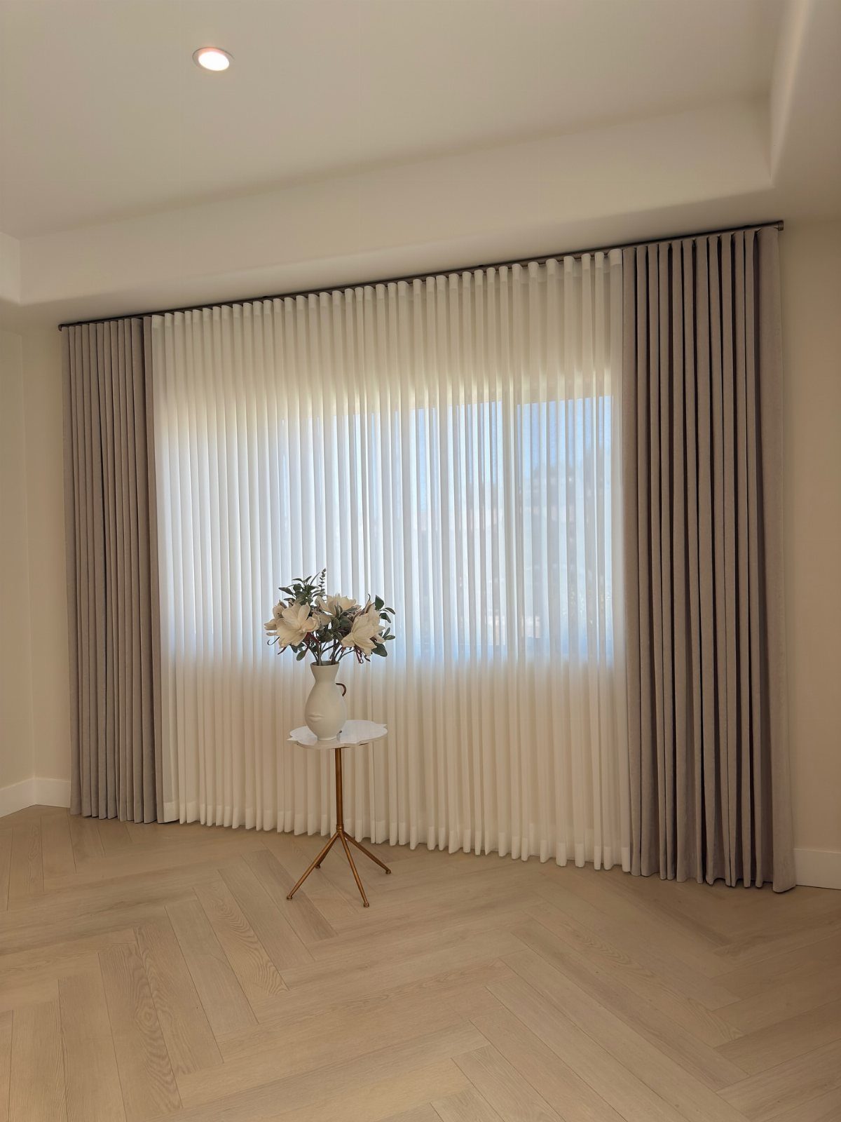 Grey and white curtains hanging from a high rod above a large window.