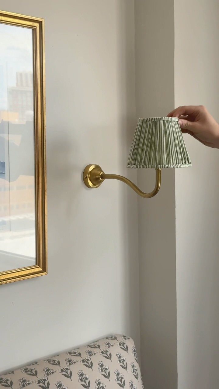 Gold wall sconce with a pleated green lampshade mounted on a white wall.