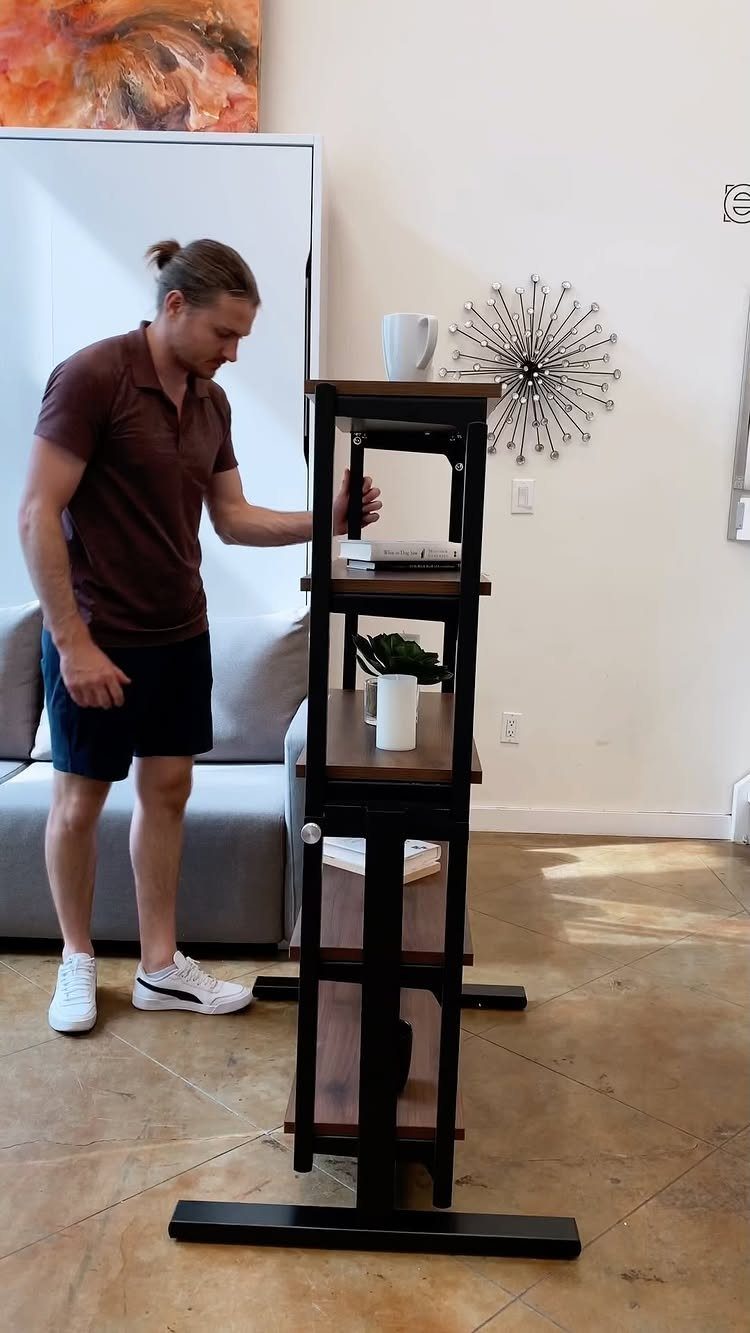 Man standing next to a tall, narrow wooden shelving unit in a modern room.