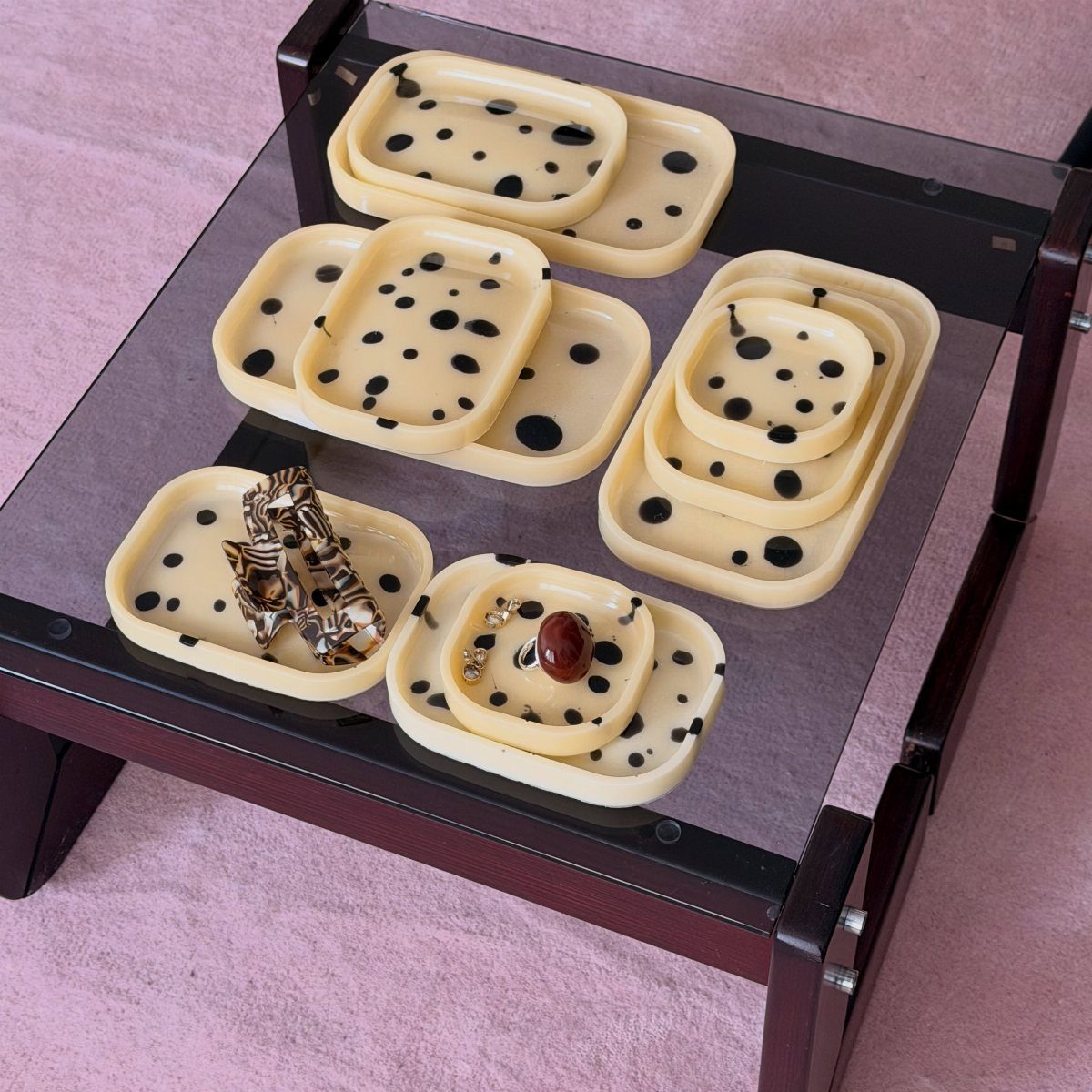 Cream polka dot trays holding jewelry on a glass coffee table over pink carpet.