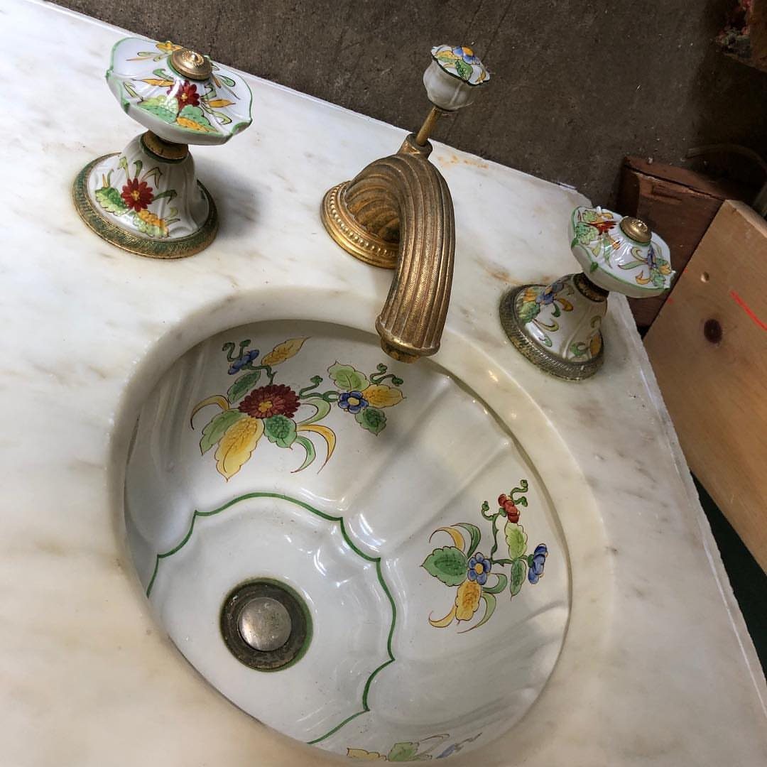 Ornate gold faucet and floral ceramic sink set into a white marble countertop.