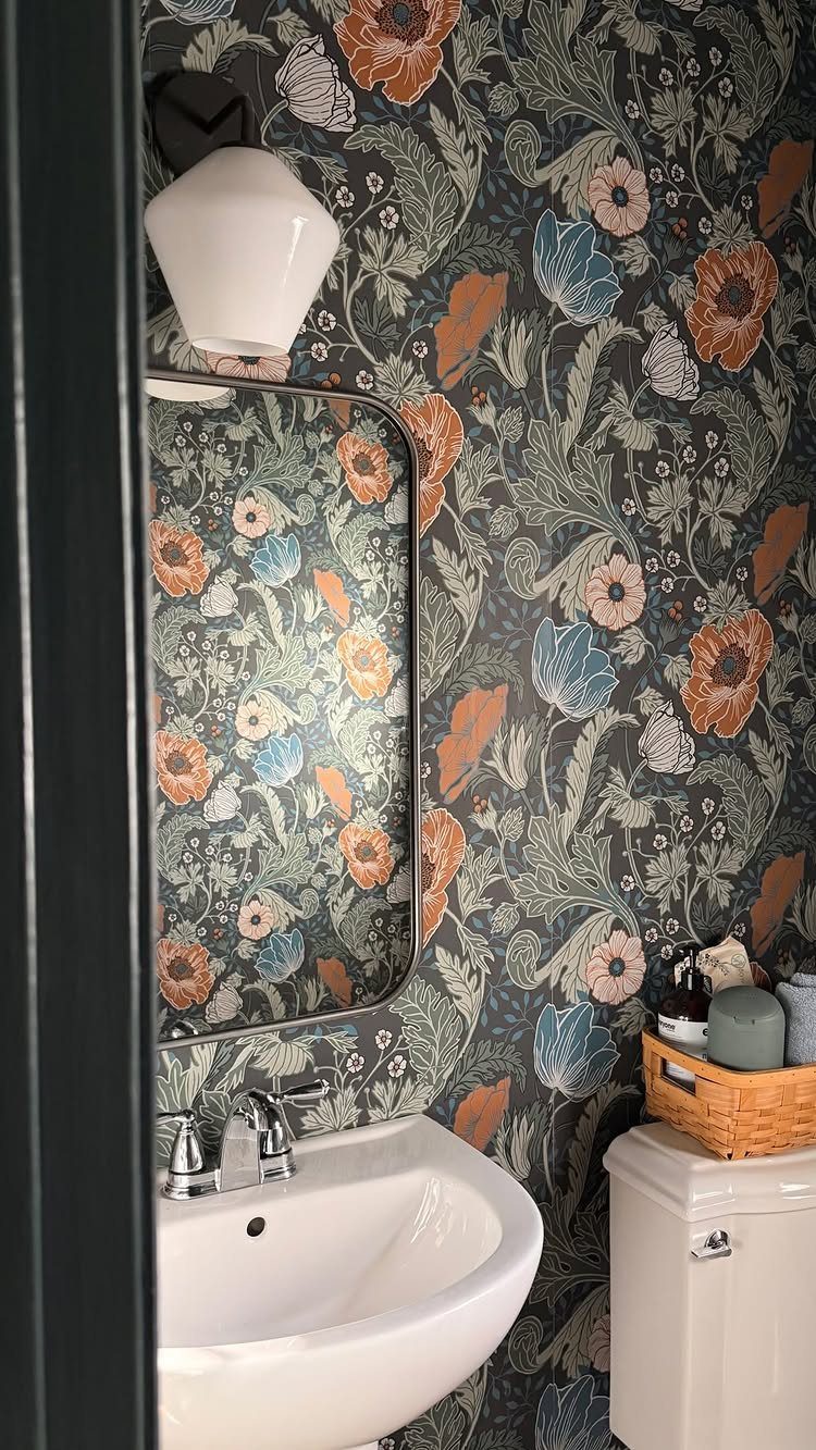 Dark floral wallpaper in a small powder room with a white sink and mirror.
