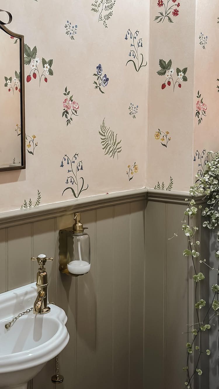 Small powder room with floral wallpaper, grey wainscoting, and gold sink fixtures.
