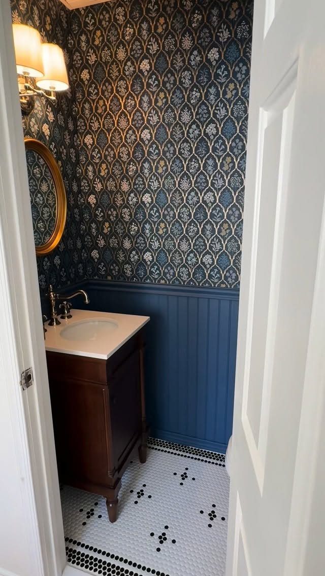Small powder room with blue patterned wallpaper, blue wainscoting, and dark wood vanity.