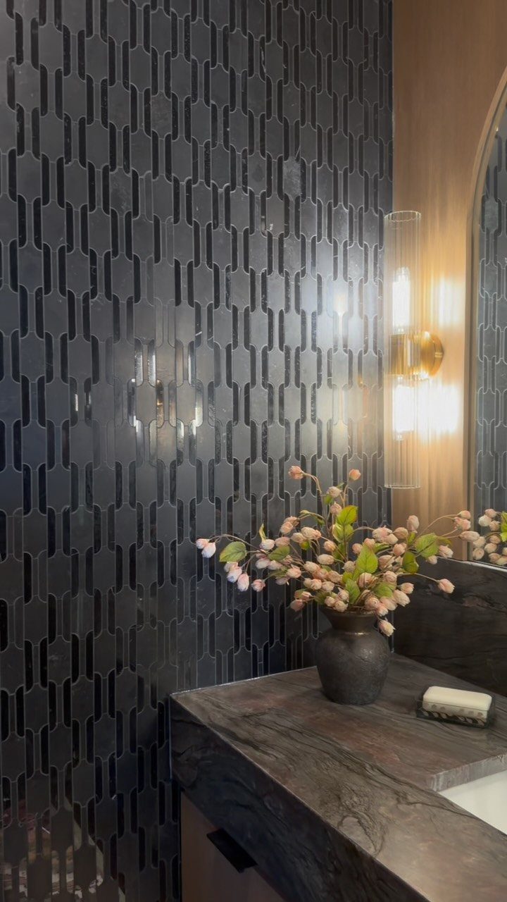 Dark glossy geometric wall tiles next to a marble counter with pink flowers.