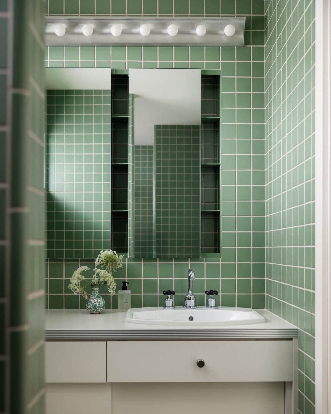 Green tiled bathroom with a white vanity and mirror with built-in side storage.
