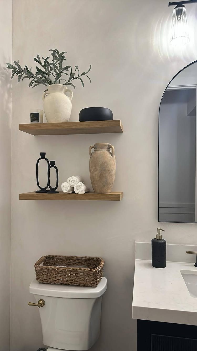 Small powder room with white walls, wooden floating shelves, and an arched mirror.