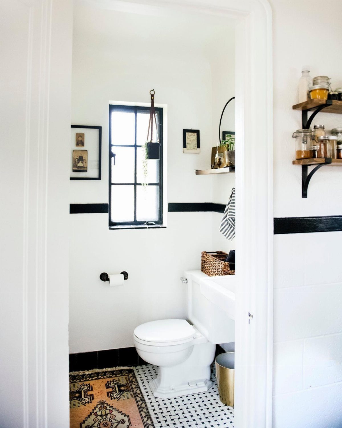 Small white powder room with black trim, patterned rug, and black-framed window.